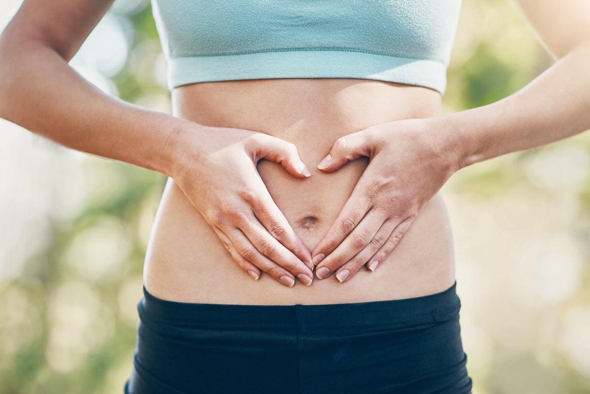 Person making a heart shape with their hands on their stomach outdoors